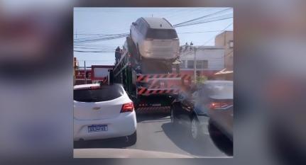 Carro de caminhão cegonha fica enroscado em fio de energia